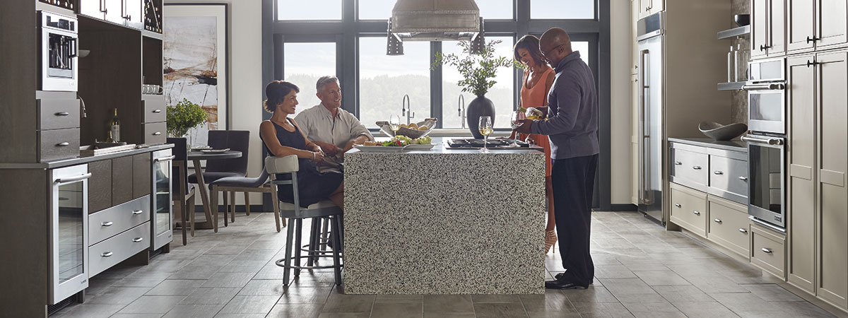 A couple entertaining guests at the island of their Omega kitchen